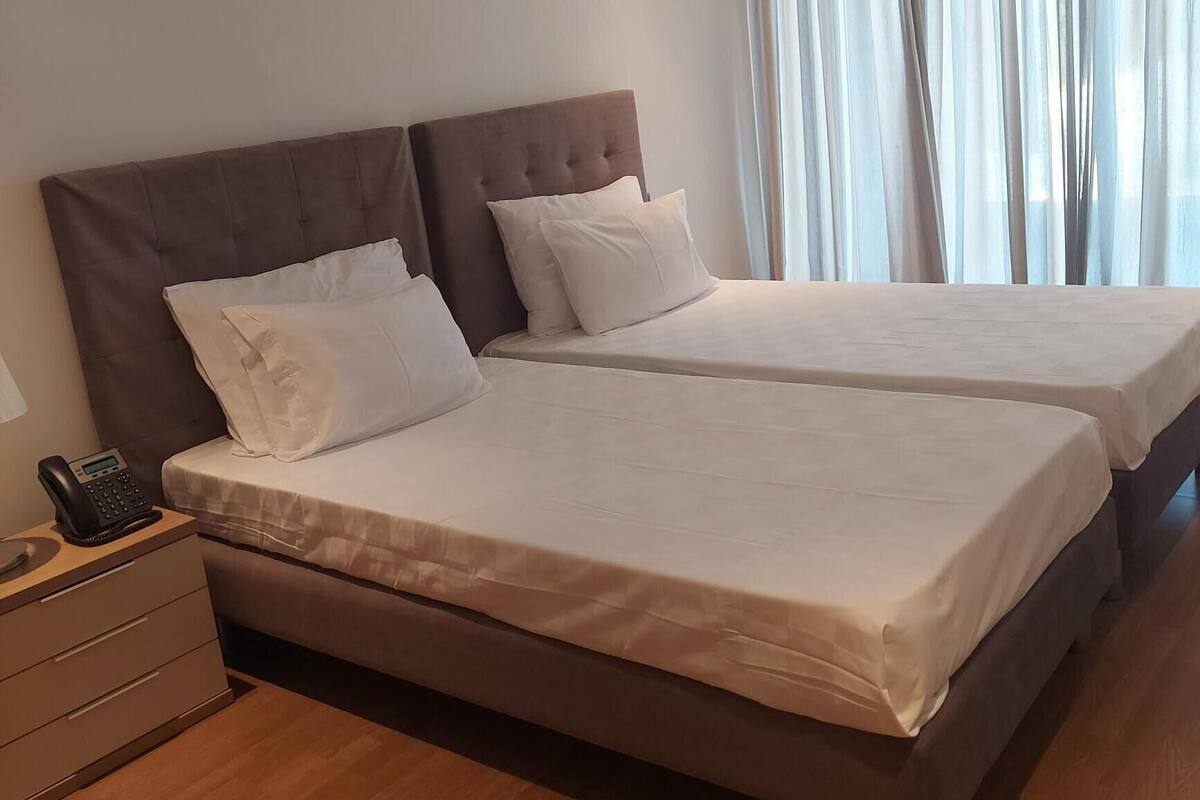 A hotel room with two beds, a bedside phone, and a window with sheer curtains.