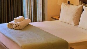 A hotel room with a neatly made bed, a nightstand with a lamp, and a window with curtains. - Hotel Cacuaco (Cacuaco)