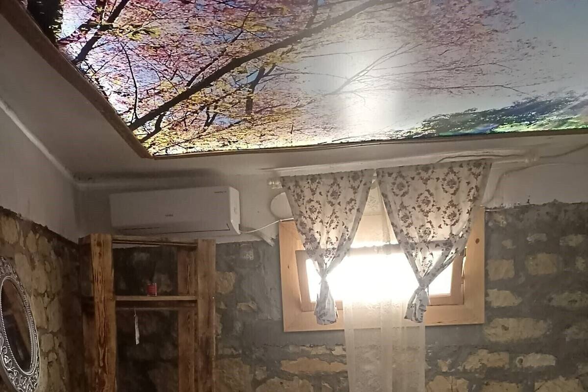 A bedroom with a stone wall, a wooden wardrobe, a bed with striped bedding, a window with curtains, and a patterned rug.