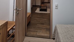 Un interior moderno con una puerta de madera que da a un cuarto con tragaluz, una lámpara de pie y una pequeña mesa.