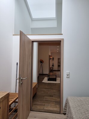 Een modern interieur met een houten deur die leidt naar een ruimte met een dakraam, een staande lamp en een kleine tafel.