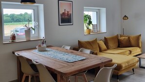 Un salón moderno con una mesa de comedor de madera, sillas blancas, un sofá amarillo y dos lámparas colgantes.