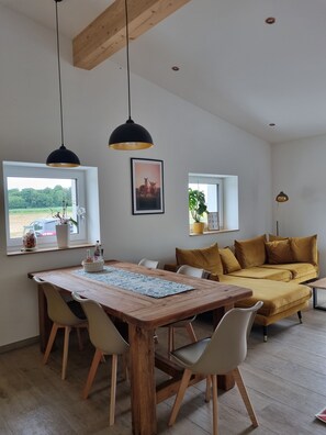 Een moderne woonkamer met een houten eettafel, witte stoelen, een geel sofa en twee hanglampen.