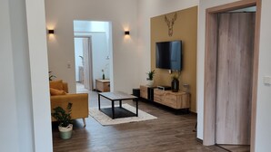 Un amplio salón con suelo de madera, un sofá, una mesa de centro y un televisor montado en la pared.