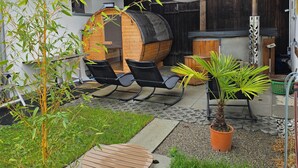Un área de estar al aire libre de estilo rústico con un barril de madera, una pequeña palmera y una manguera de jardín.