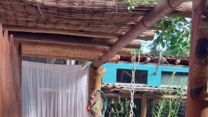 Un arc en bois rustique mène à une entrée abritée, fermée par un rideau blanc.