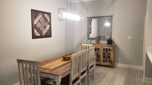 A dining area with a wooden table, chairs, a woven placemat, a chandelier, and a cabinet with a mirror.