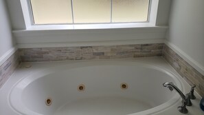 A large freestanding bathtub with a window above it, a stone tile backsplash, and a white wall.