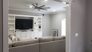 A living room with a flat-screen TV, a ceiling fan, and a sectional sofa. - Peaceful country getaway on a 2 acre pond (Folsom)