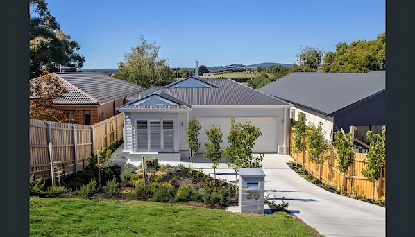 Stunning two-story house with a covered patio and beautifully maintained garden, surrounded by a wooden fence and situated in a suburban area.
