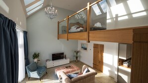 A spacious living area with a high ceiling, a chandelier, a television, a sofa, a coffee table, and a kitchen area. - Luxury one Bedroom Country Steading (Perth)