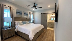 Une chambre à coucher avec un lit, des tables de chevet, un ventilateur de plafond et une vue sur la salle de bain.