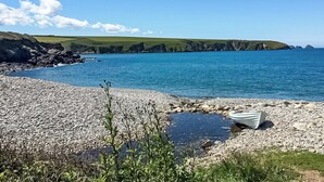 A pebble beach with a boat, clear blue sea, and grassy hills in the background. - 3 bedroom accommodation in Haverfordwest (Haverfordwest)