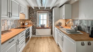 A kitchen with white cabinets, a stone accent wall, wooden countertops, and a window with a view. - 3 bedroom accommodation in Haverfordwest (Haverfordwest)