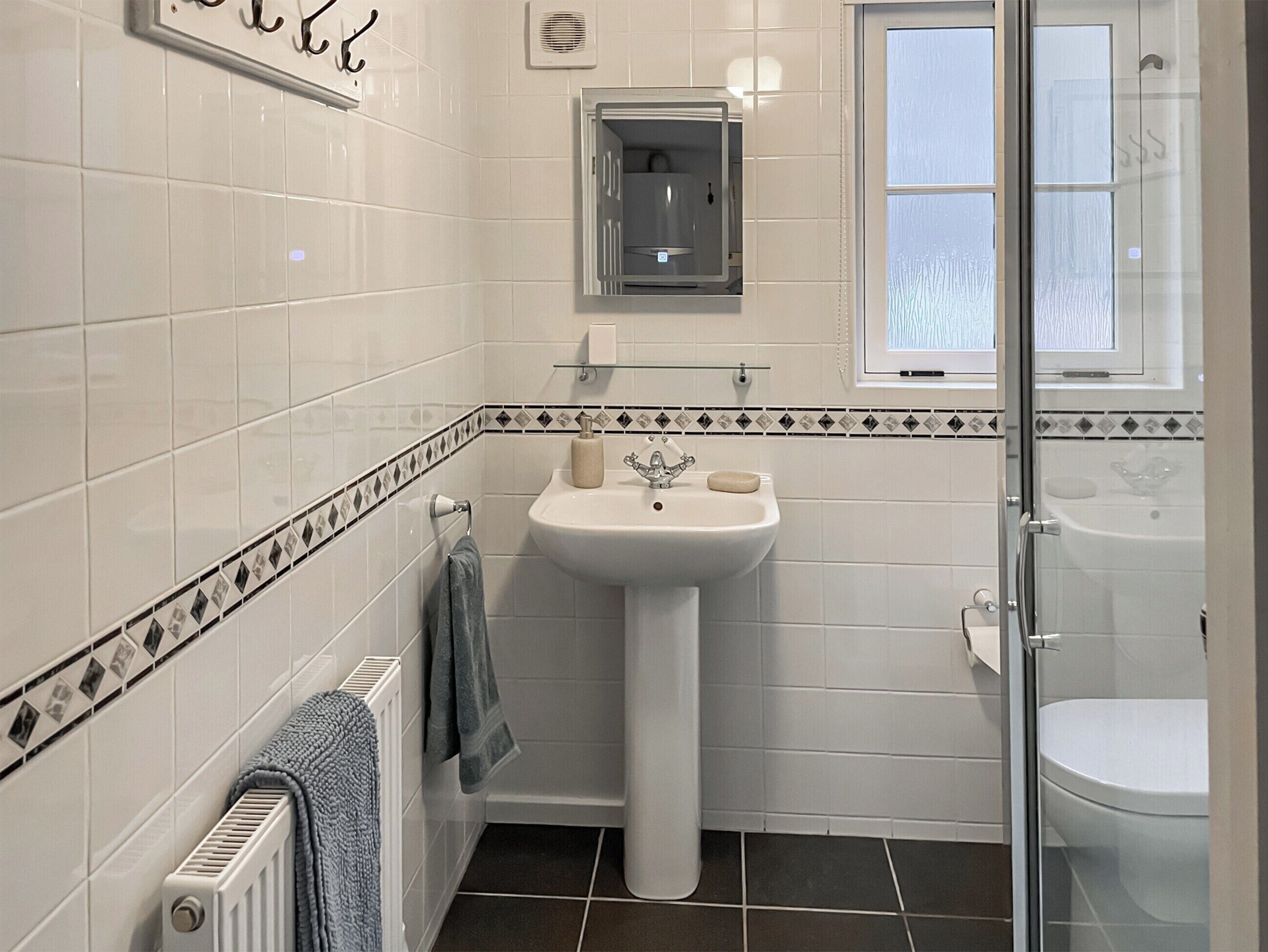 A bathroom with white tiles, a pedestal sink, a glass shower enclosure, and a toilet.