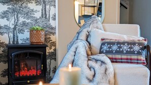 A cozy living room with a fireplace, a chair with a blanket and a snowflake pillow, and a potted plant on a mantelpiece. - Le Cémarose Charming cottage in Champagne near Epernay (Épernay)