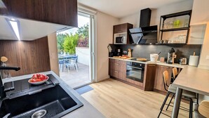 A modern kitchen with a sink, stove, and oven, a dining area with chairs, and a view of the outdoors. - Le Cémarose Charming cottage in Champagne near Epernay (Épernay)
