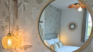 A bedroom with a round mirror, floral wallpaper, and a hanging light fixture. - Le Cémarose Charming cottage in Champagne near Epernay (Épernay)