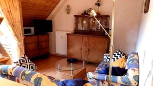Tunnelmallinen olohuone, jossa on puinen katto, lasinen sohvapöytä, kuviollinen sohva ja televisio, joka on sijoitettu kaappiin.