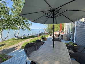 A deck with a table and chairs, overlooking a lake. - Contemporary Waterfront Home on North Lake Leelanau with Hot Tub and Dock (Lake Leelanau)