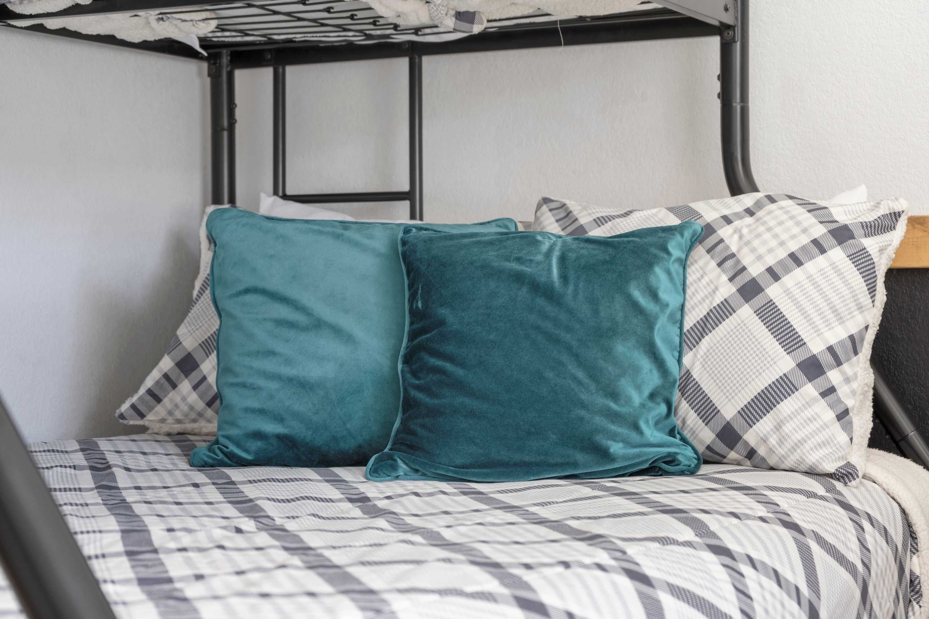 A bed with a checkered bedspread and teal pillows.
