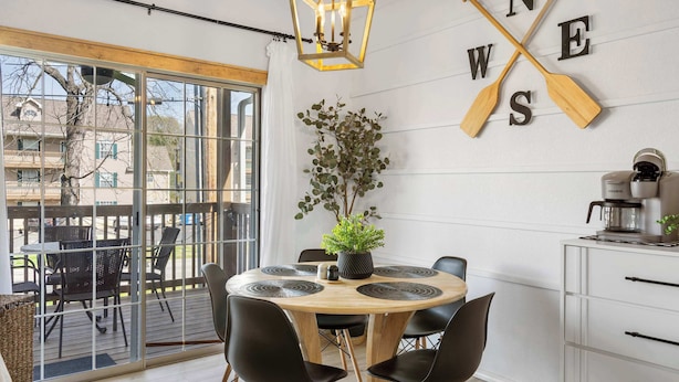 A modern dining area with a round wooden table, black chairs, a potted plant, and a wall-mounted sign with wooden paddles spelling "WES". - Our Landing Place - Access to Pool! (Branson)