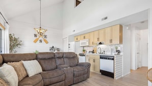 A modern living room with a brown leather sofa, a dining area with wooden cabinets, and a kitchen with white appliances. - Our Landing Place - Access to Pool! (Branson)
