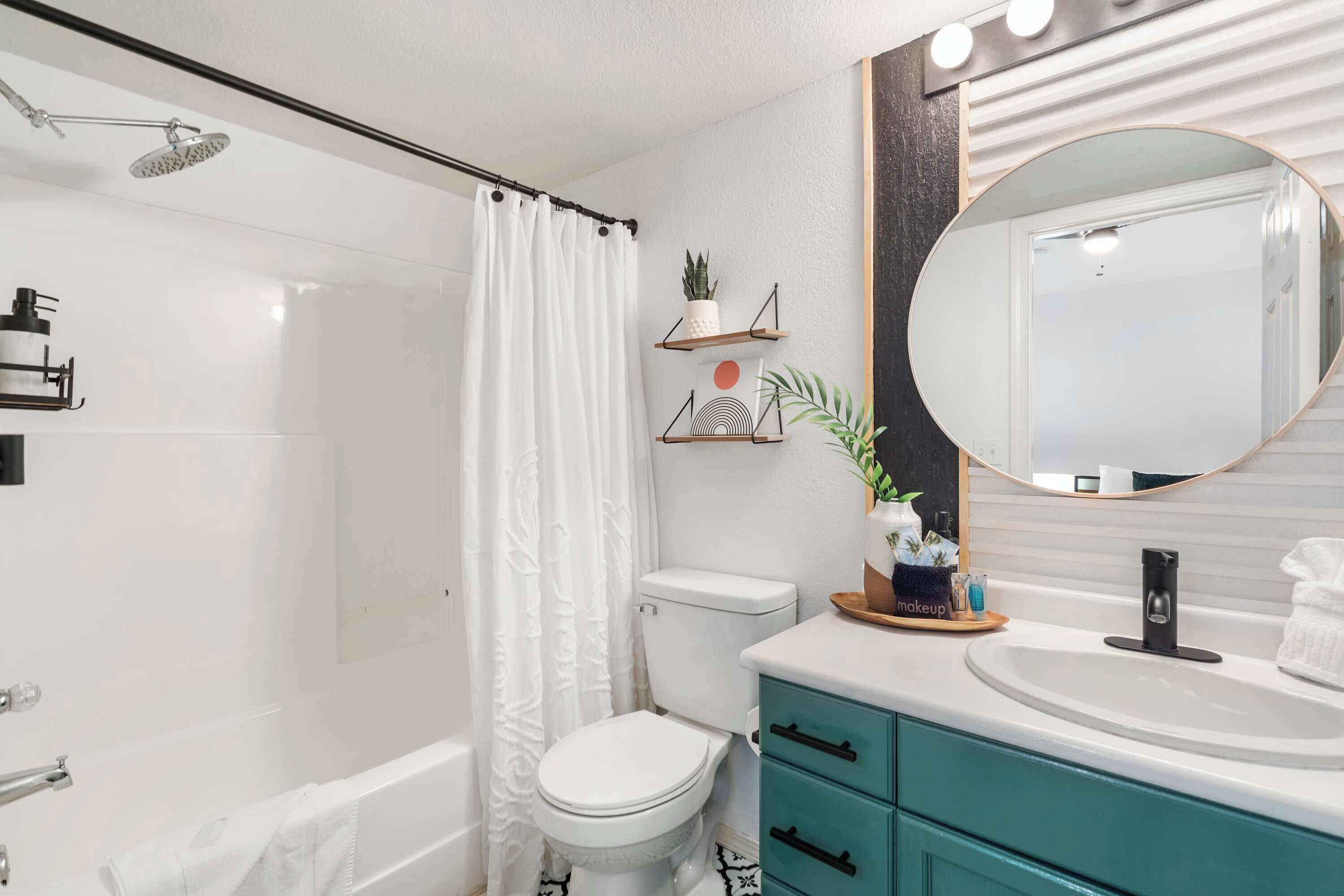 A modern bathroom with a white shower, a toilet, a sink with a mirror, and teal cabinets.
