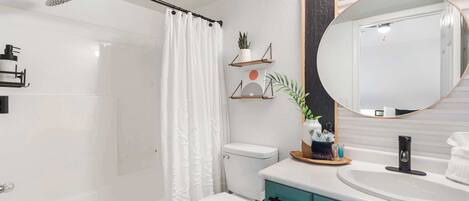 A modern bathroom with a white shower, a toilet, a sink with a mirror, and teal cabinets.
