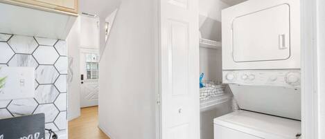Cocina compacta con cubierta blanca, salpicadero de azulejos hexagonales y una puerta blanca que da a otra habitación.