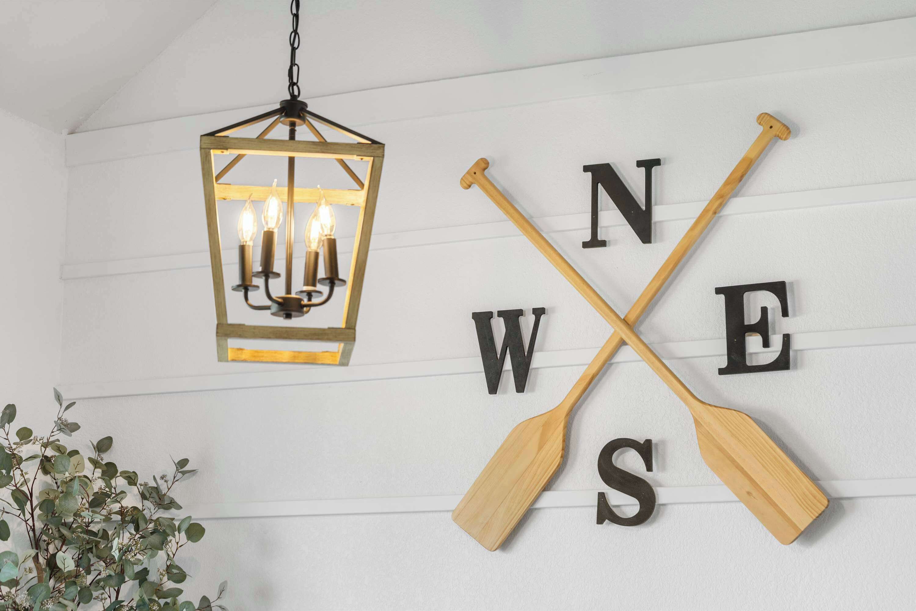 A wall with a wooden sign featuring the letters "N W E S" crossed by two wooden paddles, and a hanging lantern with three lit candles.