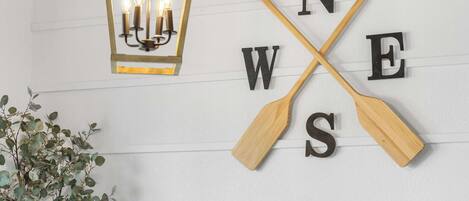 A wall with a wooden sign featuring the letters "N W E S" crossed by two wooden paddles, and a hanging lantern with three lit candles.