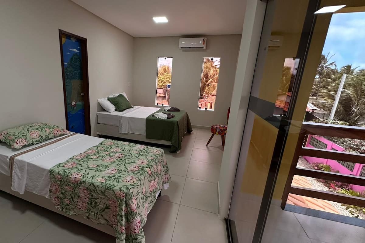 A room with two beds, a small table, and a window with a view of palm trees.