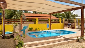 A swimming pool with a wooden deck, surrounded by a yellow wall and a wooden fence. - Pousada dos Sonhos (Rio Tinto)