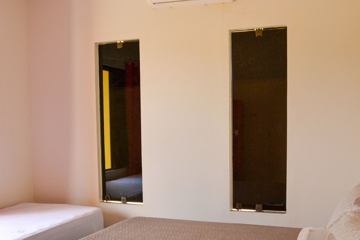 A bedroom with a single bed, a standing fan, and an air conditioning unit on the wall.