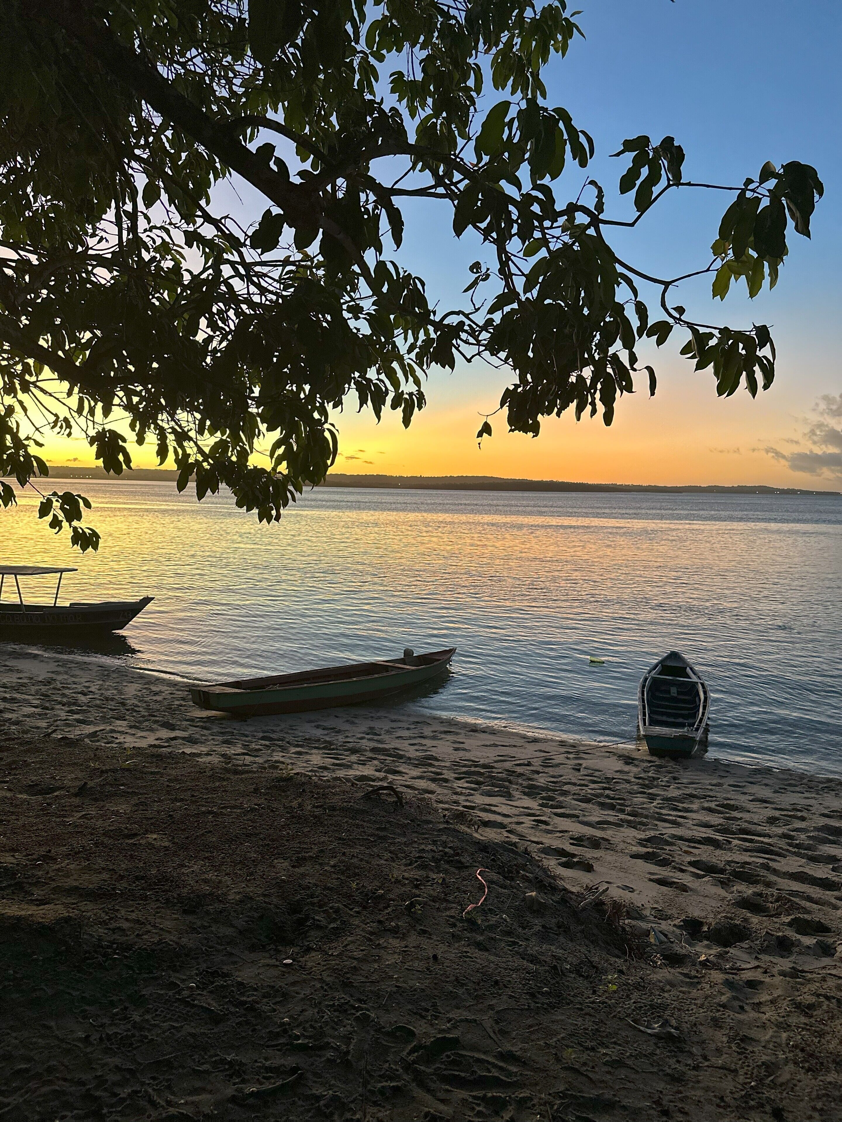 Una playa con barcos y un mar tranquilo bajo un cielo al atardecer.