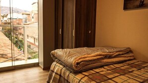 Ein Schlafzimmer mit großem Fenster, einem Bett mit Karo-Bettdecke und einem Holzschrank.