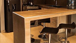 Eine moderne Küche mit Holzausstattung, einem schwarzen Kühlschrank, einer Mikrowelle, einem Herd und einem Wasserspender. Zwei Barhocker mit Metallfüßen sind vorhanden.