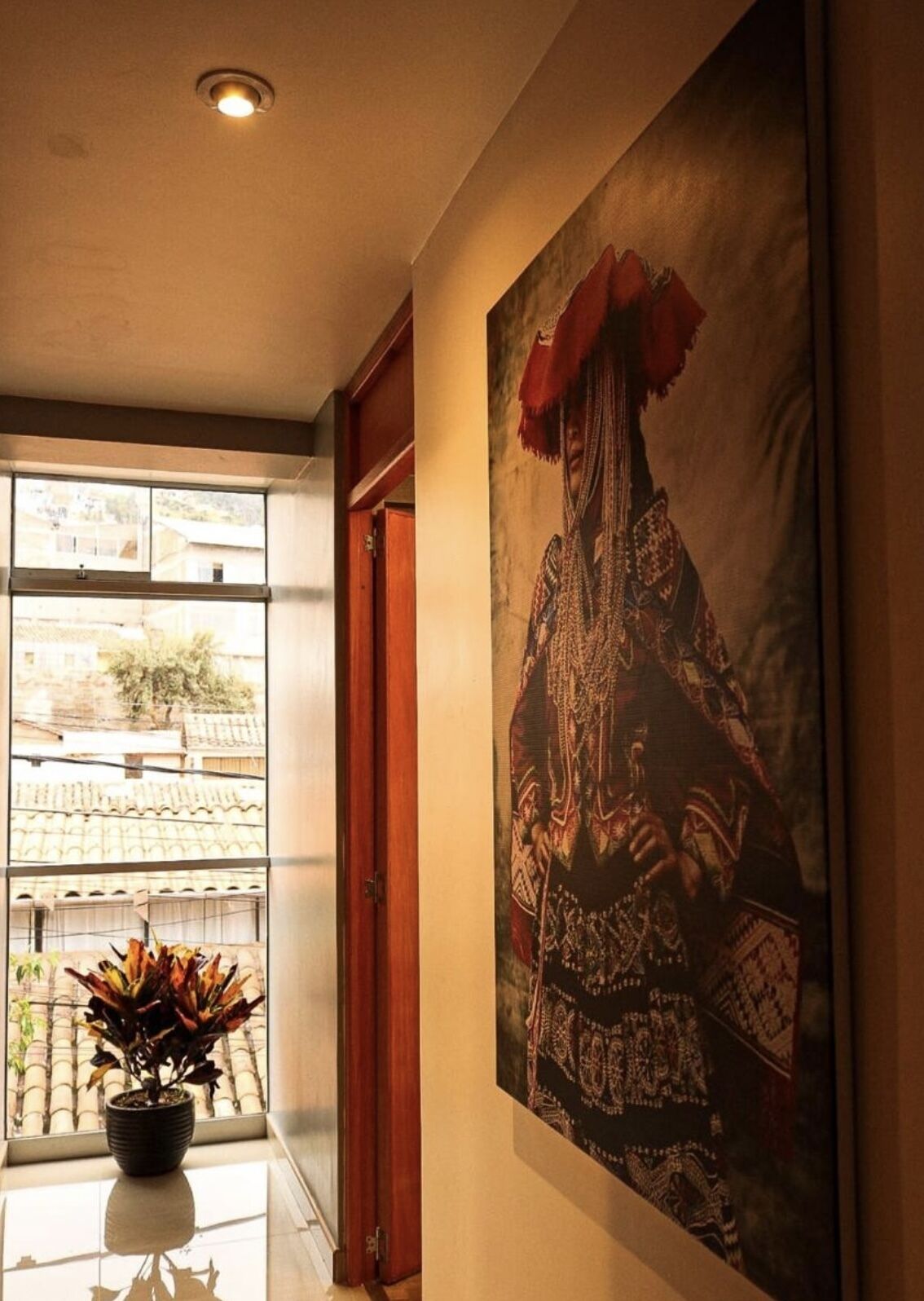 A hallway with a large window, a potted plant, and a framed artwork on the wall.
