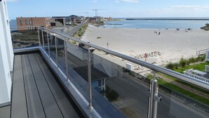 Un balcon avec vue sur une plage, des bâtiments et une étendue d’eau.