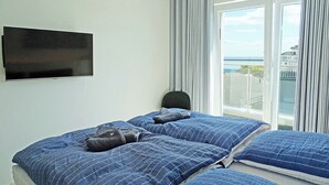 Une chambre d’hôtel avec un lit, un téléviseur fixé au mur et une vue sur la mer par la fenêtre.