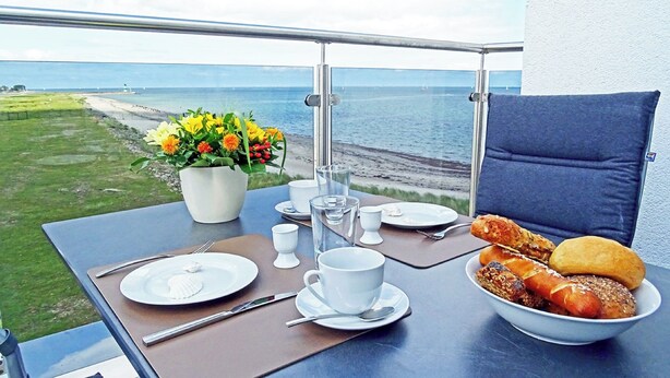 Une table de balcon avec vue sur la mer, un vase de fleurs et un bol de nourriture.