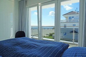 Una camera d'albergo con un'ampia finestra che si affaccia sulla spiaggia e su un edificio dall'altra parte dell'acqua.