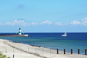 Une plage avec un phare, un voilier et une clôture qui longe le rivage.