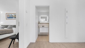 A modern hotel room with a bed, a desk, a bathroom with a mirror and sink, and a door leading to another room. - Strandkrabbe - 1st row on the water & beach, ground floor, shower room, terrace (Olpenitz)