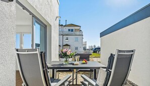 An outdoor patio with a table and chairs, a vase with flowers, and a view of a building in the background.