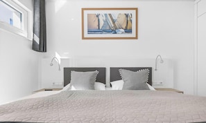 A modern bedroom with a large bed, two bedside tables, a painting above the bed, and a window on the left.