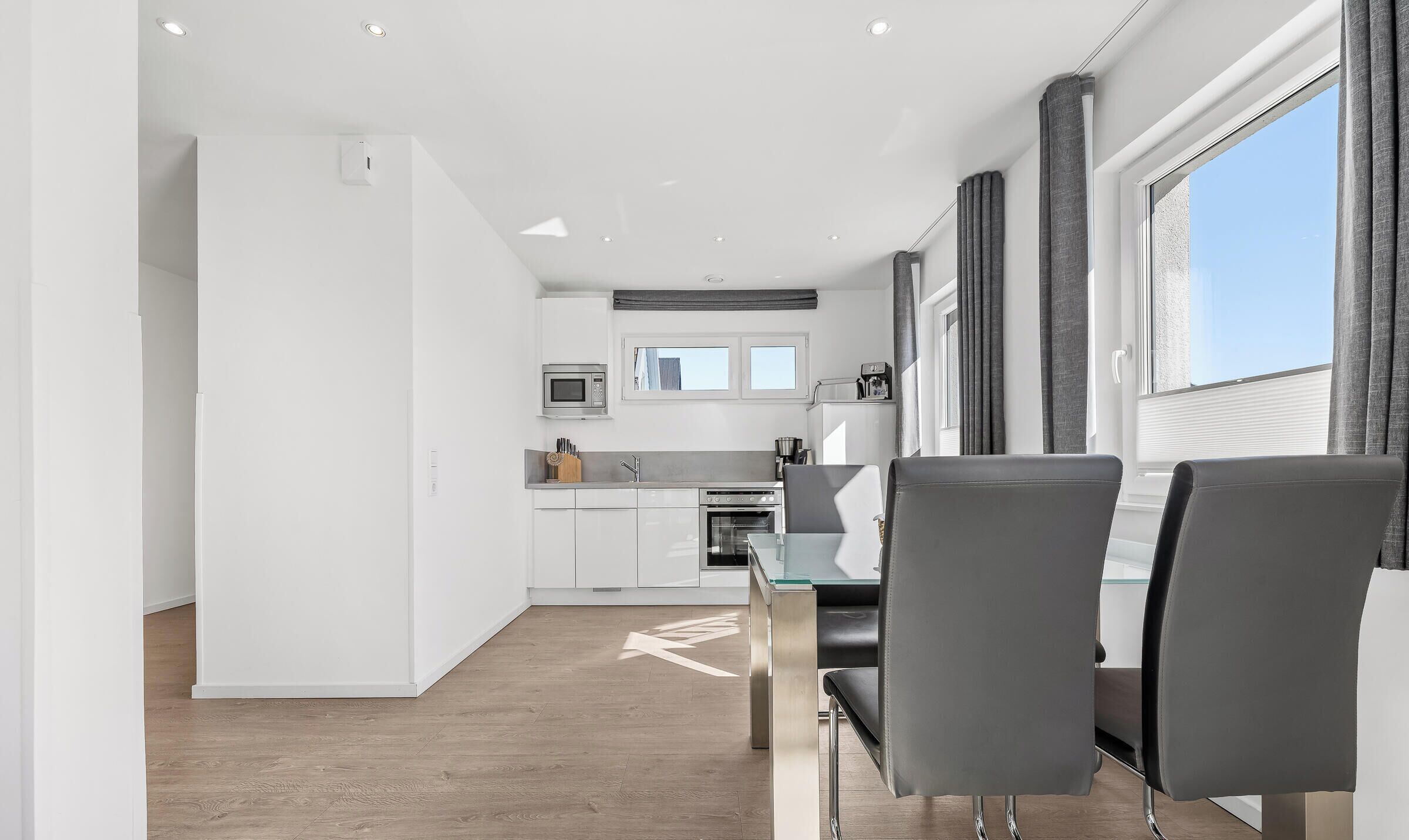 A modern kitchen with white cabinets, a microwave, and a stove. There is a dining area with a table and chairs.