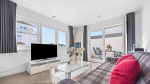 A modern living room with a flat-screen TV, a glass coffee table, a sofa with a plaid cover, and a balcony with a dining area. - Strandkrabbe - 1st row on the water & beach, ground floor, shower room, terrace (Olpenitz)