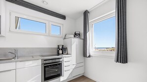 A modern kitchen with a built-in oven, a coffee machine, and a view of the beach. - Strandkrabbe - 1st row on the water & beach, ground floor, shower room, terrace (Olpenitz)